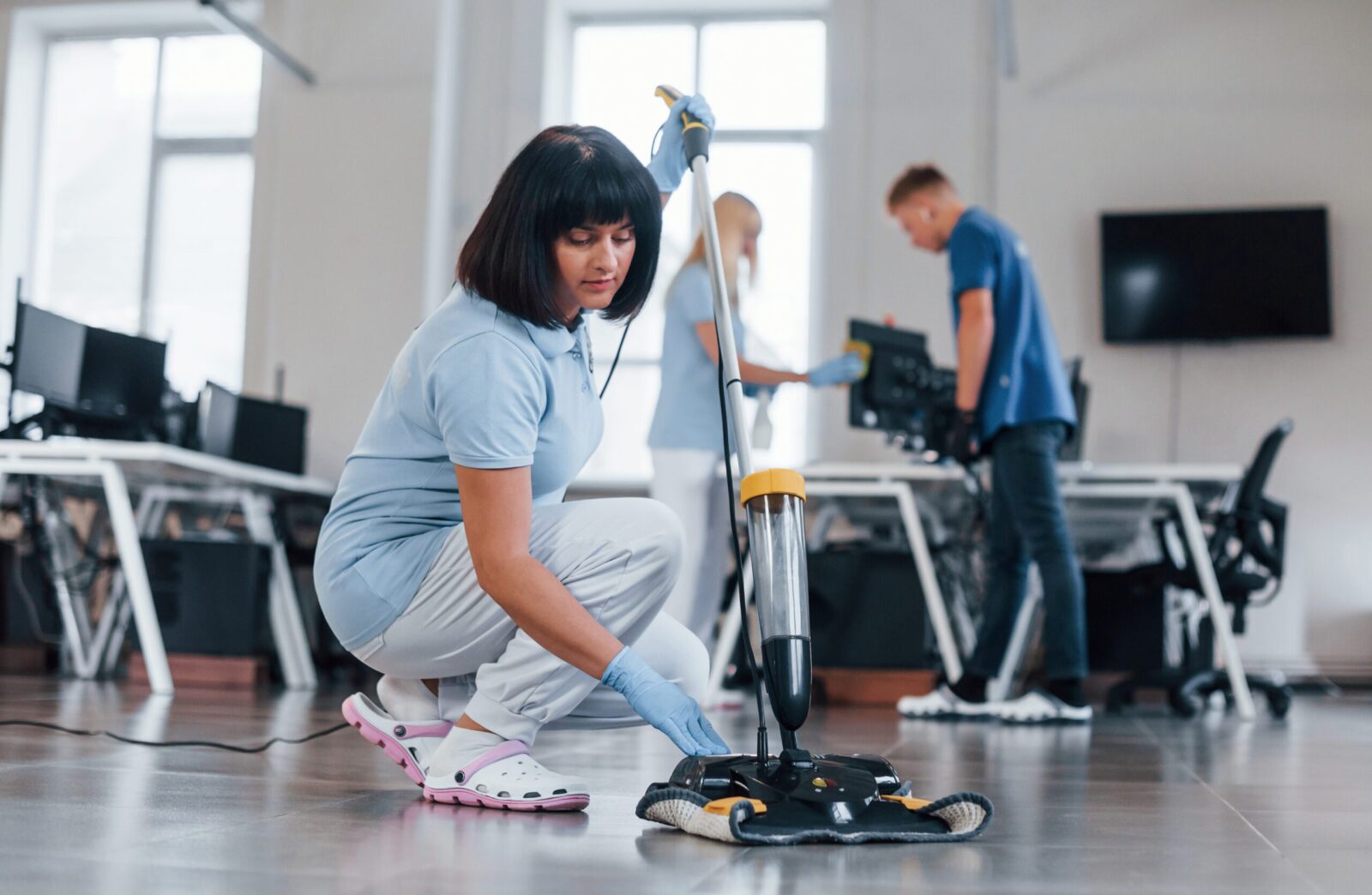 a woman holding a mop and 2 people behind her cleaning